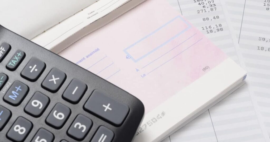 Gros plan d'une calculatrice posée sur un carnet de chèques ouvert et des fiches de paie.